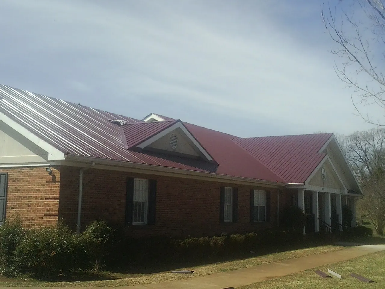 Red metal roof with gabled entries on a long brick building, from a Hail Damage Roof Repair job in Mabton