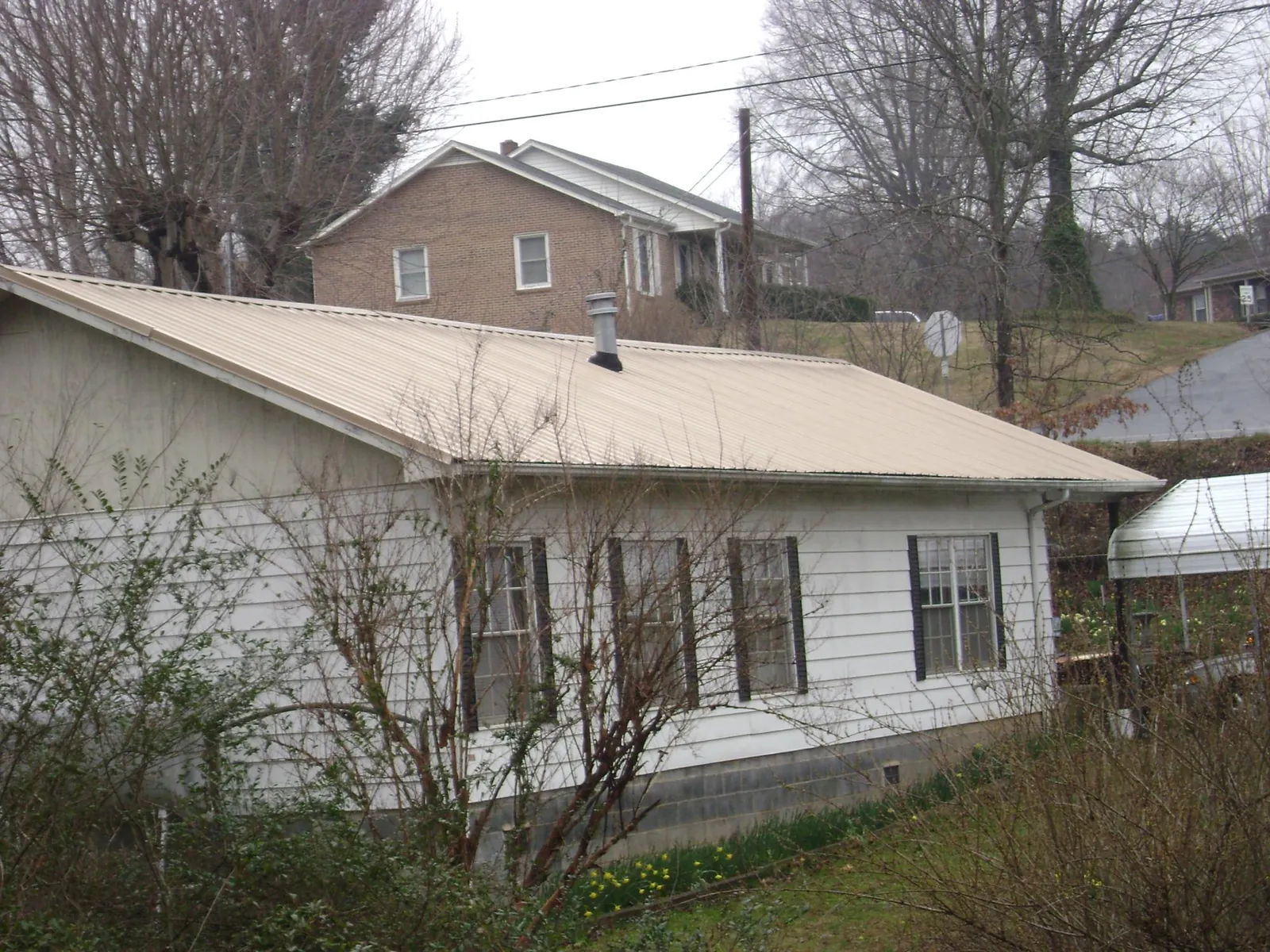 Tan metal roof on a white sided house set into a hillside — Commercial Roofing by Roofing Brothers in Mabton